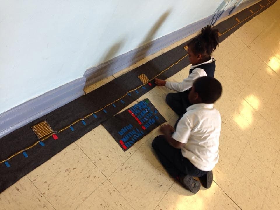 Two children working with Montessori bead chain materials on the classroom floor
